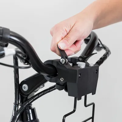 Mano che aziona la leva di fissaggio su supporto nero montato sul manubrio di una bicicletta, con struttura in metallo visibile.