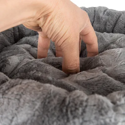 Ruka tiskne měkký, šedý plyšový materiál, ukazuje polstrování a texturu produktu.