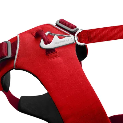 Фрагмент красной шлейки для собак с металлическим карабином и надписью Ruffwear, видны регулируемые ремни и кольцо для поводка.