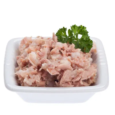 Valkoisessa keraamisessa kupissa annos vaaleaa, paloiteltua lihaa ja persiljan oksa päällä. Tuotemerkki tai tarkempi sisältö ei näkyvissä.