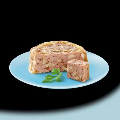 Detailní záběr na masovou paštiku s kouskem na modrém talíři, ozdobenou petrželí.