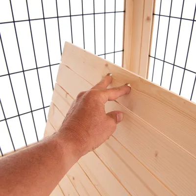 Main posée sur une paroi en bois clair devant une structure à grille métallique noire, montrant le matériau et l’assemblage du produit.