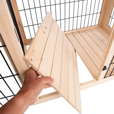 Main tenant une étagère en bois amovible à l’intérieur d’une cage avec structure en métal et bois, montrant le montage ou démontage du plateau.