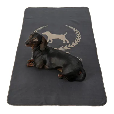 Crni jazavčar leži na tamnosivoj deki s otiskom psa i lovorovog vijenca. Materijal izgleda kao tkanina.