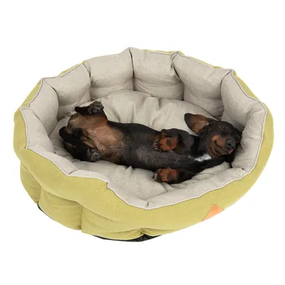 Hundeseng i beige og lysegrøn stof med lille sortbrun hund, der ligger på ryggen i sengen. Synlig polstring og blød kant rundt om hele sengen.