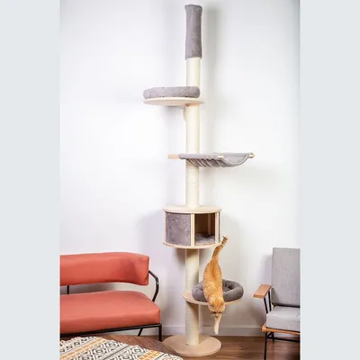 Tiragraffi alto con più piattaforme e cuccia in tessuto grigio, struttura in legno e sisal, un gatto arancione scende dalla base imbottita. Mobili visibili sullo sfondo.