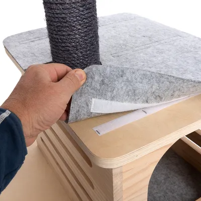 Hånd viser aftageligt filtbetræk med velcrolukning på en træoverflade ved siden af et kradsetræ af sisal.