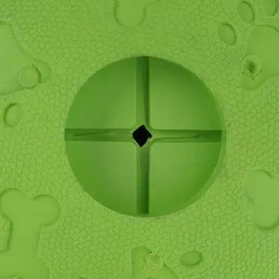 Dettaglio di un gioco verde per animali in plastica con superficie a rilievo, ossa e impronte visibili, foro centrale a croce.