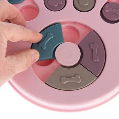 Pink interactive toy with movable parts in bone shape, hand demonstrates use by sliding a green element.