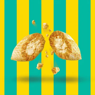 Zwei aufgebrochene Snacks mit knuspriger Hülle und cremiger Füllung, umgeben von kleinen Bruchstücken vor gelb-türkis gestreiftem Hintergrund.