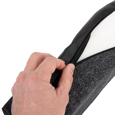 Close-up of a hand opening a zip on a cushion. Shows removable cover made of fabric and faux leather.