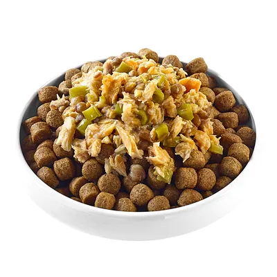 Bol blanc contenant des croquettes brunes pour animaux, garnies de morceaux visibles de viande et de légumes verts. Aucun emballage ou marque n’est visible.