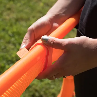 Hand befestigt ein orangefarbenes Klettband an einer gerippten Kunststoffstange, geeignet für den Aufbau von Trainings- oder Spielgeräten.