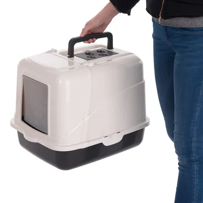 Person trägt eine geschlossene Transportbox mit schwarzem Boden und hellem Deckel am Griff. Sichtfenster mit Pfotenmuster an der Vorderseite.