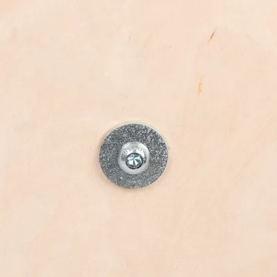 Vista detallada de un tornillo de metal con arandela sobre madera clara.