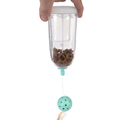 Distributore di cibo trasparente con palla verde e cibo per gatti, tenuto da una mano. Giocattolo che combina alimentazione e intrattenimento.
