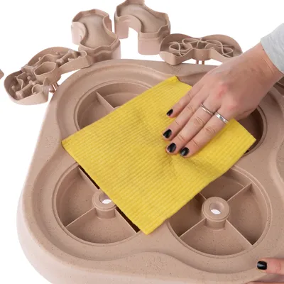 Hand torkar av ett beige aktivitetsbräde i plast med en gul trasa. Flera lösa delar syns ovanpå brädet.