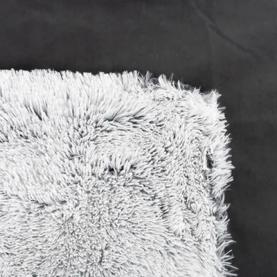 Nahaufnahme einer grauen, flauschigen Textur auf schwarzem Hintergrund. Material möglicherweise Kunstfell oder Mikrofaser.