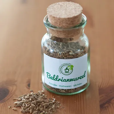 Glazen fles met kurksluiting, gevuld met valeriaanwortel. Etiket toont 'Baldrianwurzel' en logo met vermelding van gecertificeerde ingrediënten. Fabrikant: Aurnüller, Korbwaren, Michelau.