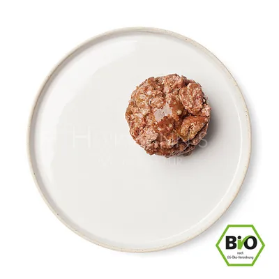 Cibo umido biologico certificato su piatto bianco, Herrmann's Manufaktur. Sigillo biologico secondo regolamento CE visibile.