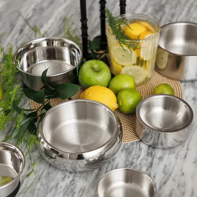 Több rozsdamentes acéltál különböző méretekben, citromokkal, lime-okkal és almákkal egy márványasztalon.