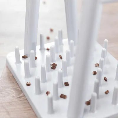 Valkoinen muovinen aktivointilelu, jossa useita pystysuoria tappeja ja ruskeita herkkupaloja niiden välissä