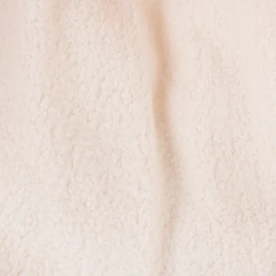 Detailní záběr na krémově zbarvenou, měkkou látku s nadýchanou texturou.