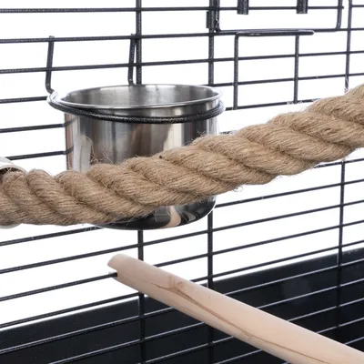 Close-up view of a cage accessory with stainless steel bowl, sisal rope and wooden perch attached to a metal grid.