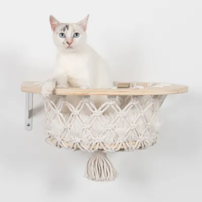 Wandhängendes Katzenbett aus Holz und Makramee mit Quaste, montiert an Metallhalterungen.