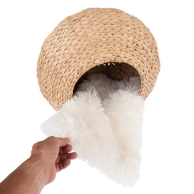 Căsuță împletită din material natural cu pernă detașabilă din blană artificială albă. Mâna arată scoaterea pernei.