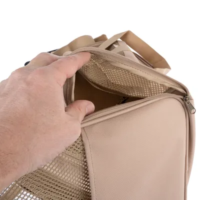 Sac de transport beige pour animaux, tissu et filet, fermeture éclair ouverte montrant l’intérieur. Main tenant le rabat supérieur en filet.