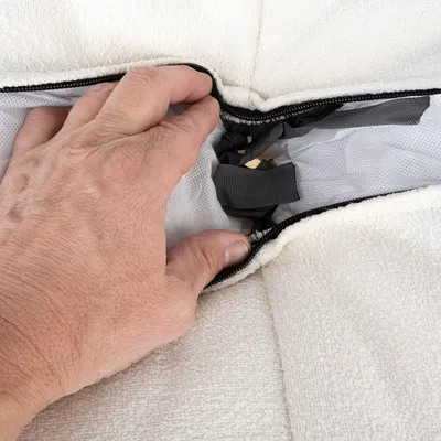 Mano abre la cremallera de una funda de tela blanca, mostrando correas y material de malla debajo.