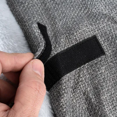 Nahaufnahme eines grauen Stoffmaterials mit Klettverschluss, der von einer Hand geöffnet wird.