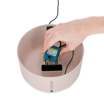 Mână arată instalarea unei pompe submersibile într-o fântână de băut bej cu filtru.