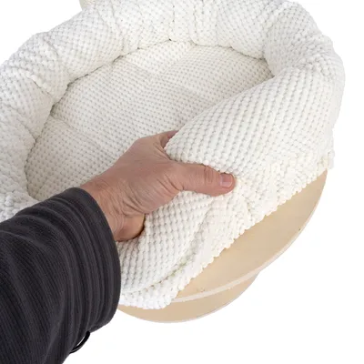 Hand hebt weiches, weisses, strukturiertes Polster von einer Holzplattform. Detailaufnahme der Materialbeschaffenheit.
