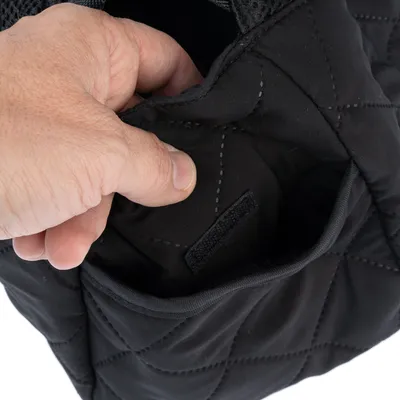 Close-up of a black bag with quilted seams, showing a hand opening a small outer pocket with a hook-and-loop fastener.