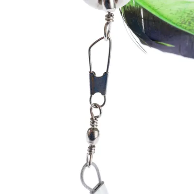 Primer plano de un colgante de juguete con clip de metal, bolas plateadas y pluma verde.