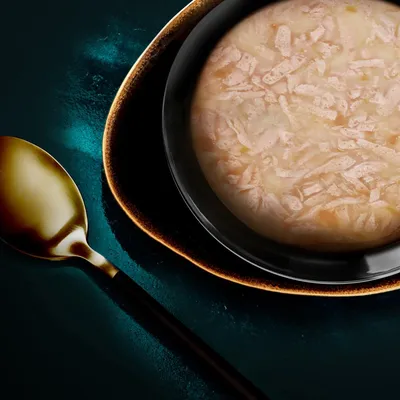Close-up of a bowl with shredded wet food, beige colour, served on a dark plate. Golden spoon next to it.