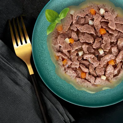 Chunks of meat in gravy with small pieces of carrot and potato served on a green plate, garnished with fresh basil.