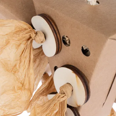 Jouet pour animaux en carton avec disques en bois et lanières de papier, plusieurs trous visibles sur la surface du jouet.