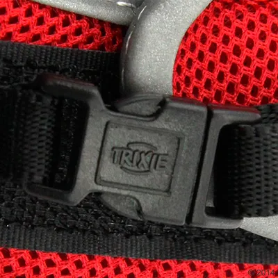 Close-up of a black plastic buckle with the word 'TRIXIE' on it, attached to a red mesh material and black strap.