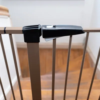 Säkerhetsgrind med metallstänger och svart låsmekanism, installerad vid toppen av en trappa.