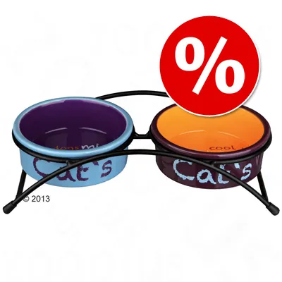 Dos cuencos de cerámica para gatos con soporte metálico, uno azul y otro naranja, texto visible: Cat's. Símbolo de porcentaje en círculo rojo indicando oferta o descuento.