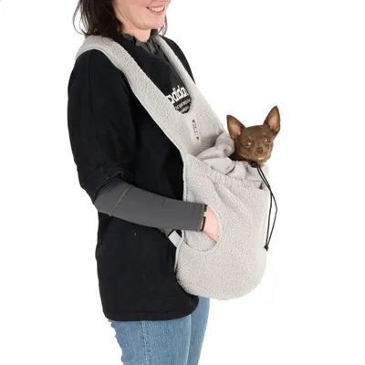 Femme portant un petit chien marron dans un sac de transport gris en tissu polaire, bandoulière réglable et cordon visible. Marque 'goldpaw' partiellement lisible sur le t-shirt.
