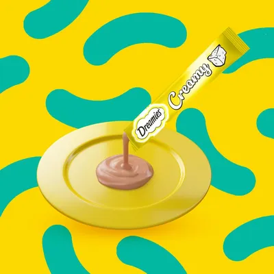Creamy treat being squeezed from a Dreamies Creamy tube onto a yellow plate, showing product texture and serving suggestion.