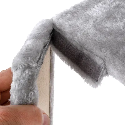 Nahaufnahme einer grauen, weichen Stoffabdeckung mit Klettverschluss auf einer Holzplatte. Hand zeigt die Befestigungsmethode.