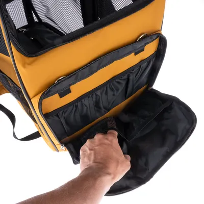 Sac de transport jaune pour animaux avec poche avant zippée ouverte, compartiments intérieurs visibles et main accédant à la poche. Parties en tissu et filet noir.