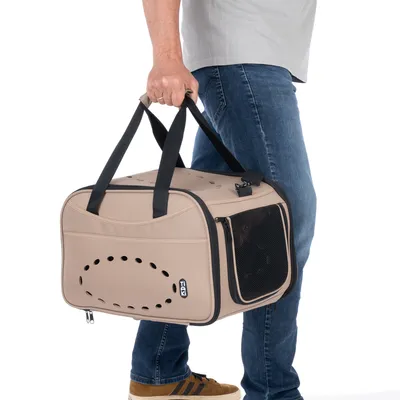 Sac de transport beige TIAKI avec poignées noires, côtés en tissu et filet, porté à la main par une personne en jean et t-shirt gris. Aérations visibles sur le côté.