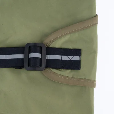 Détail d’une sangle noire avec bande réfléchissante et boucle en plastique sur tissu vert, couture visible. Matériaux : tissu synthétique, plastique.