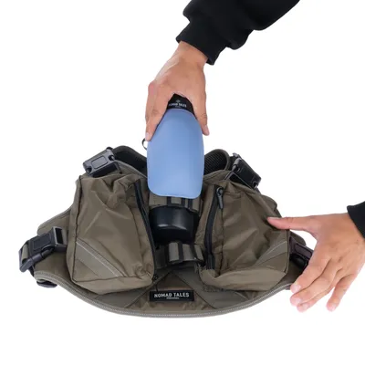 Nomad Tales Hundegeschirr mit Taschen, zeigt eine Hand, die eine blaue Trinkflasche in die Halterung einsetzt.